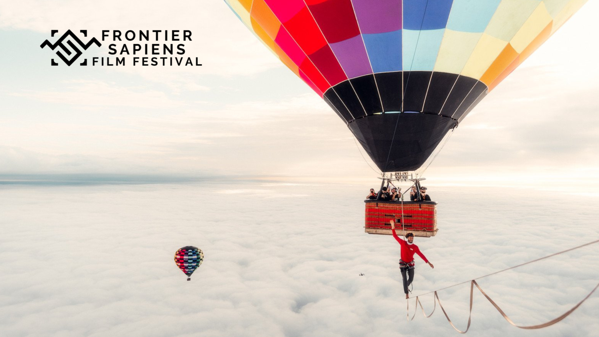 A hot air balloon floats above the clouds as a man walks across a tightrope that is being suspended from the balloon. The Frontier Sapiens Film Festival can be seen. 
