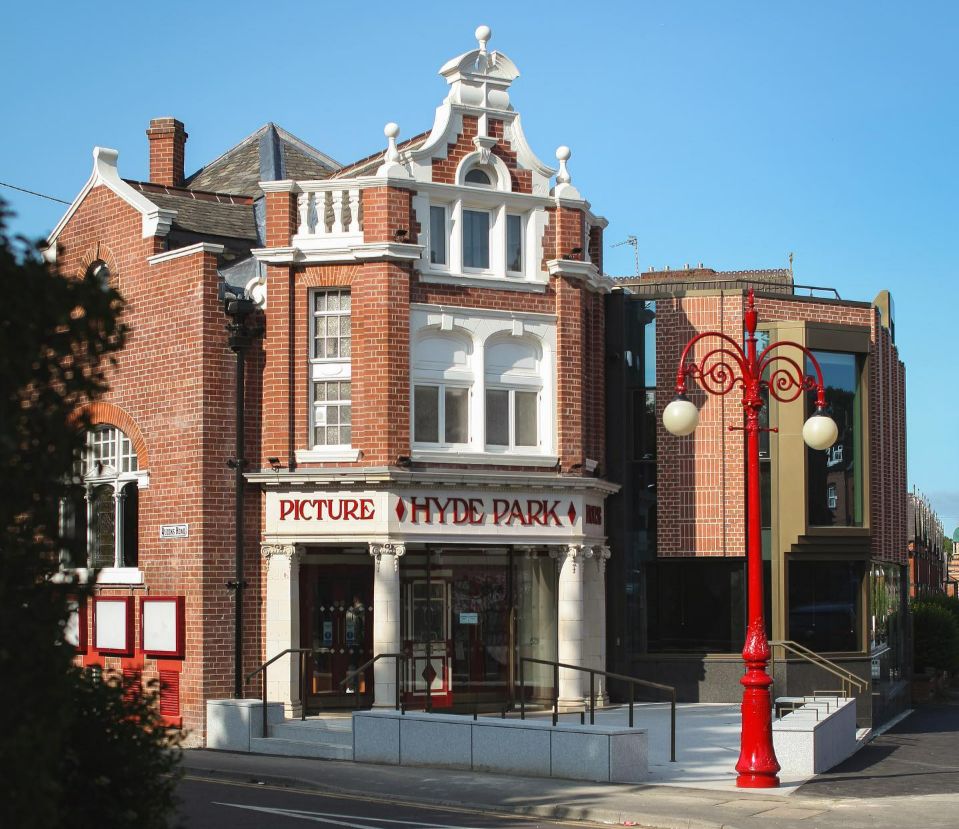 An old brick cinema with an old fashioned red lamppost and a newer looking extension on the right. It says HYDE PARK PICTURE HOUSE.
