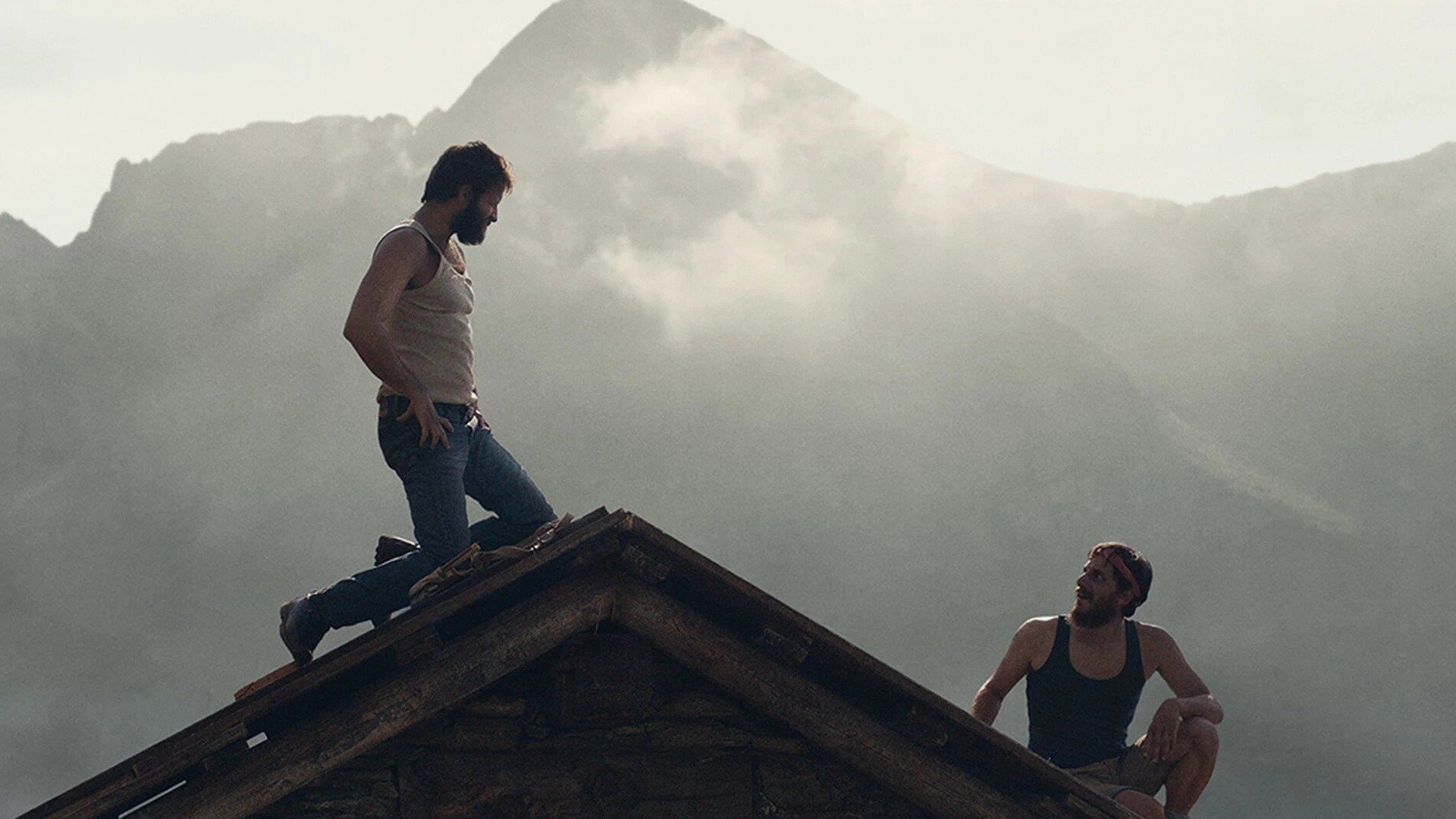 Two man sit on top of a wooden roof, a huge misty mountain dominating the background behind them, 