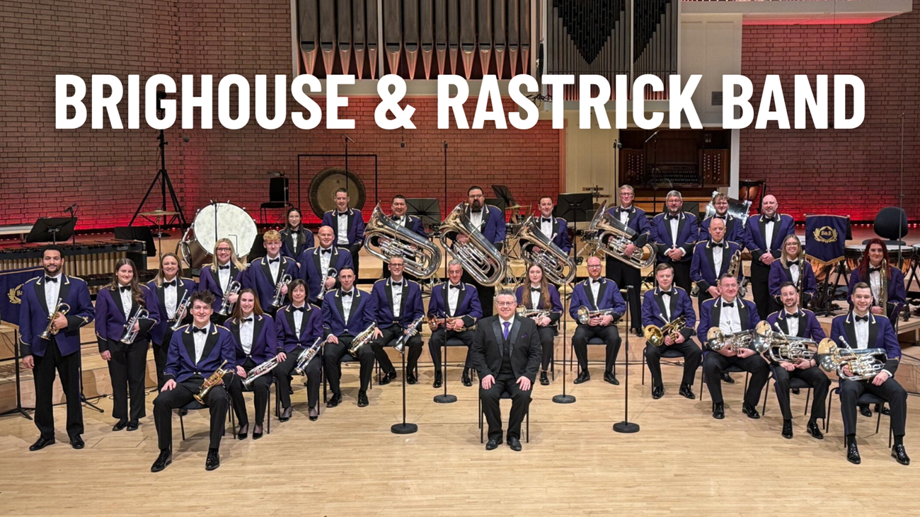 Members of the Brighouse & Rastrick Band in their purple suit concert dress uniform sat in formation with their brass instruments. They are sat in front of a pipe organ.