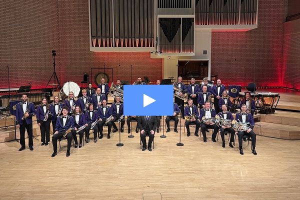 Members of the Brighouse & Rastrick Band in their purple suit concert dress uniform sat in formation with their brass instruments. They are sat in front of a pipe organ.