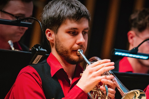 A young man in red and black concert dress playing a cornet.