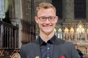 A young man with glasses in black tie concert dress smiling.