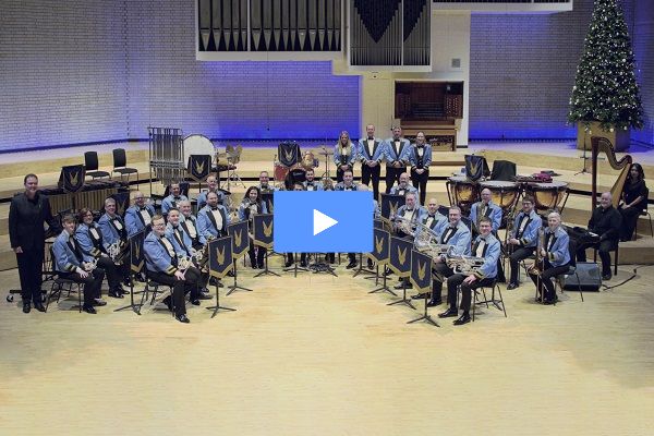 A brass band on stage in concert dress performing.