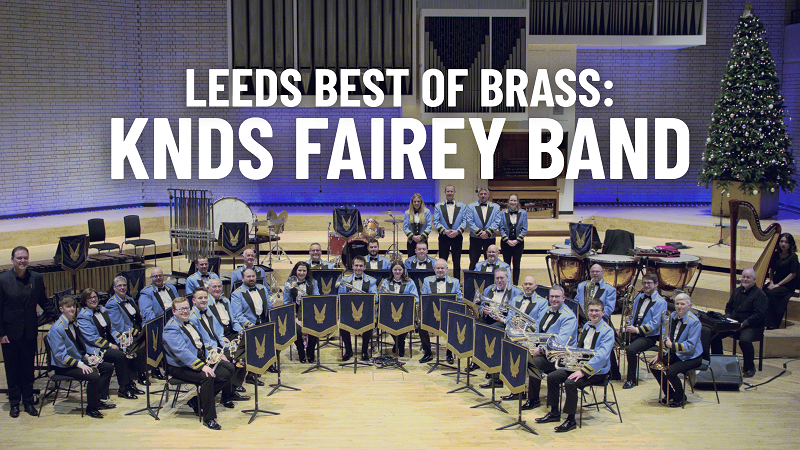 KNDS Fairey Band title image. A brass band in blue concert dress with their instruments on stage in formation.