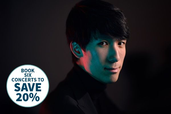 Pianist Eric Lu in a black high-collared top with different coloured lights on his face.
