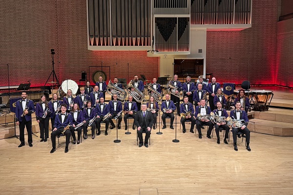 Members of Brighouse & Rastrick Band in purple concert dress in formation in a concert hall with their instruments.