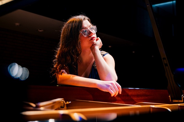 Pianist Madeleine Brown sat at a piano with one hand on her chin and the other leant over the open grand piano.