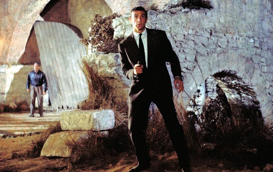 A stylish man in a suite holds a gun, ready to leap into action. 