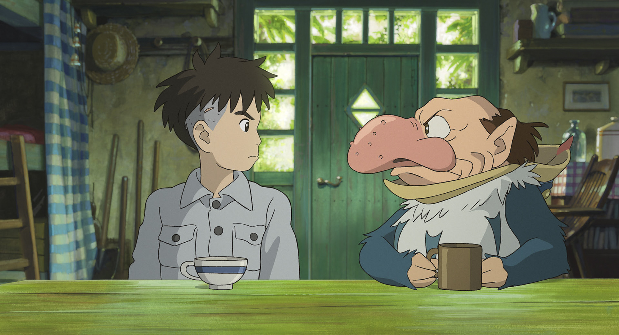 An animated image of a young man sat in a country kitchen next to a bird-like man with a huge beak like nose. They are both staring at each other, with mugs of tea sit in front of them. 