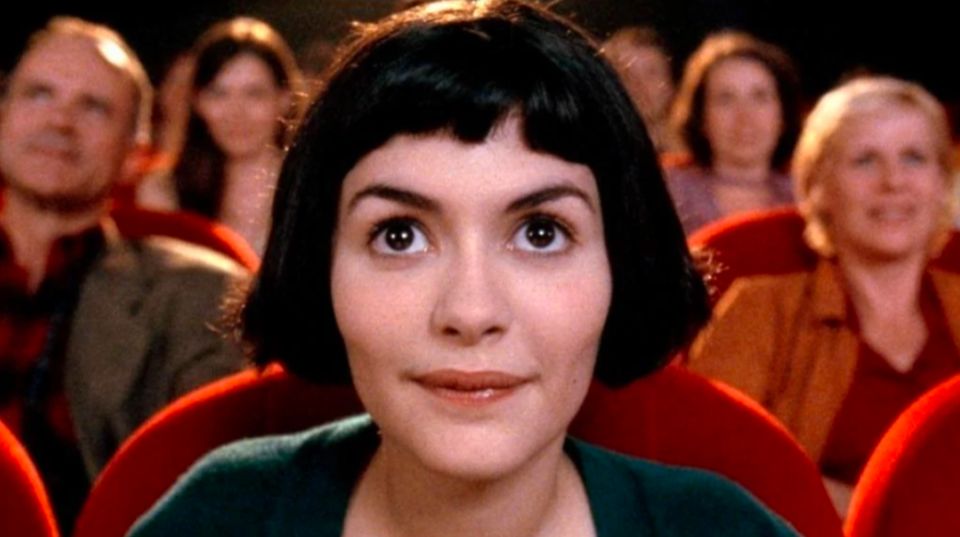 A young woman with a black bob cut, sits in a cinema with an enraptured look on her face.