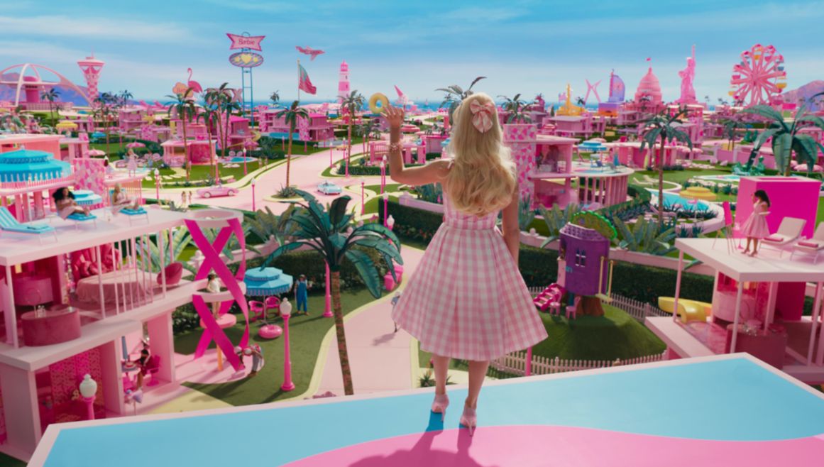 Barbie stands on top of her pink dreamhouse looking at the colourful, pink and plastic world she lives in.