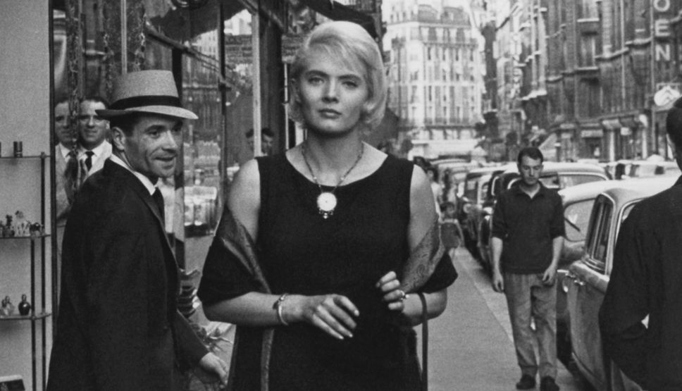 A glamourous woman walks down the street in 60's Paris, turning heads.