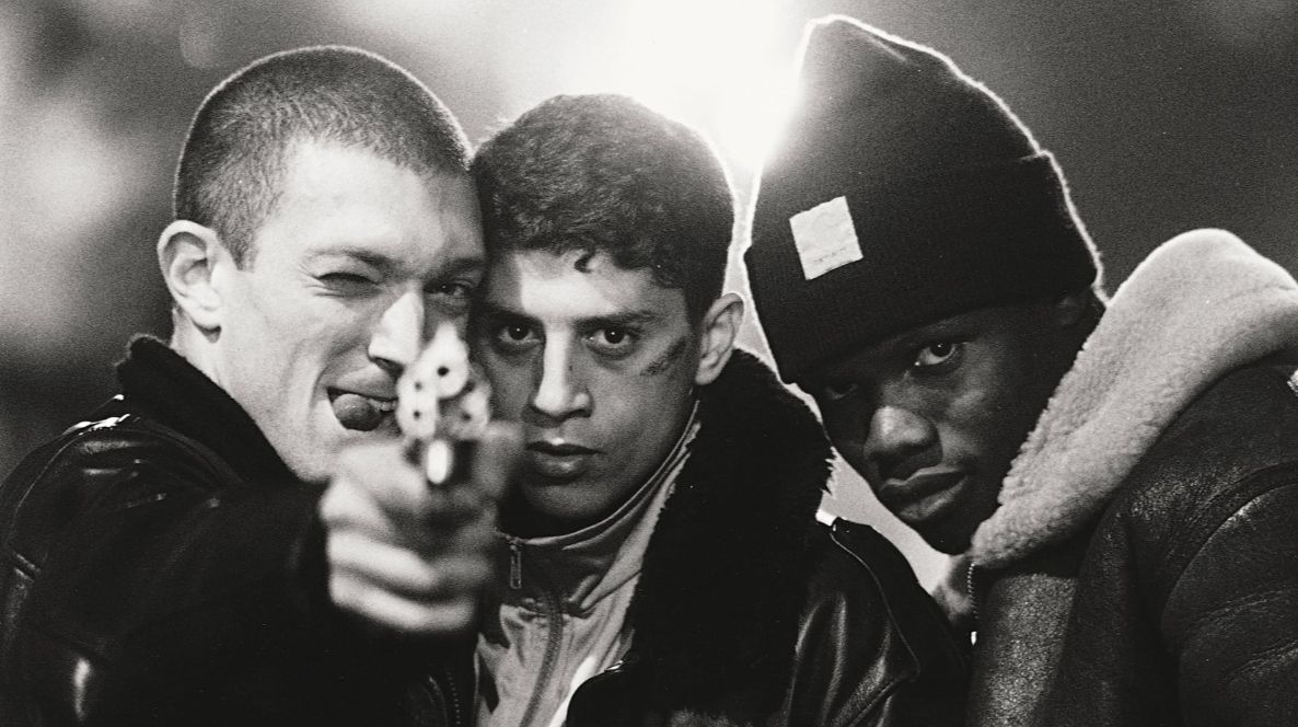 Three young man pose for the camera, looking touch and holding a gun.