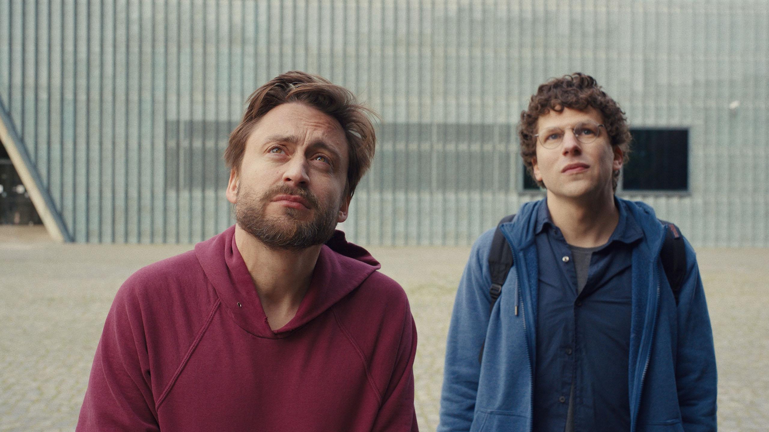 Two young men in scruffy clothing look up at something past the camera. 