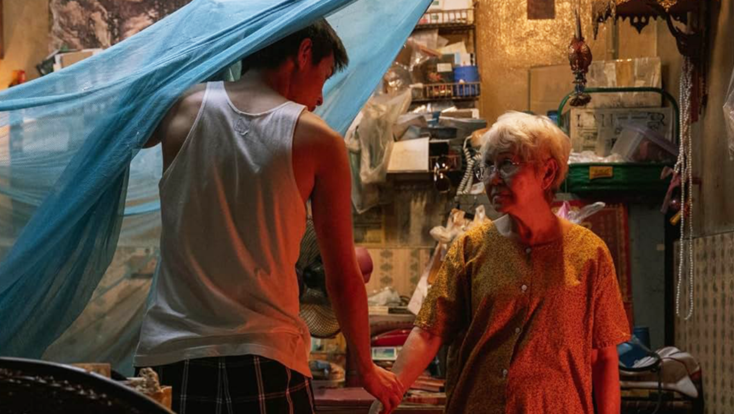 A young man in a vest holds the hand of his elderly grandmother. 