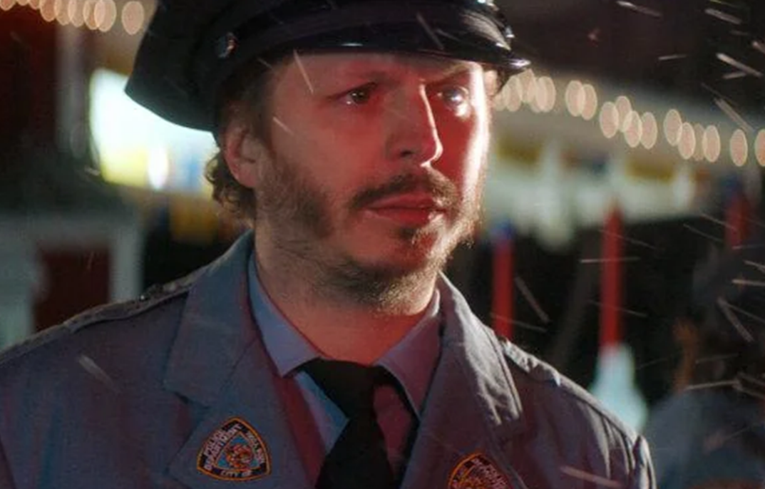 Michael Cera stands in the snow, wearing a police uniform and with tears in his eyes. 