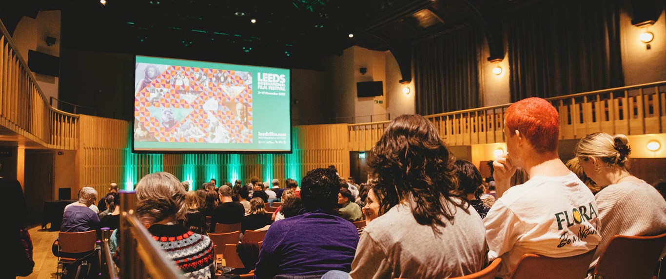 An audience of people sit in a large auditorium, looking at the LIFF logo on screen. 