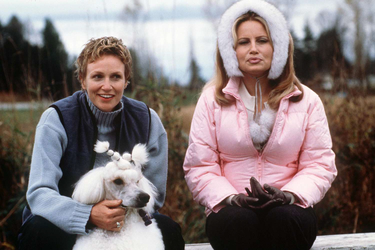 Two women sitting outdoors with a white poodle, dressed in winter clothing, in a still from the comedy film Best in Show.