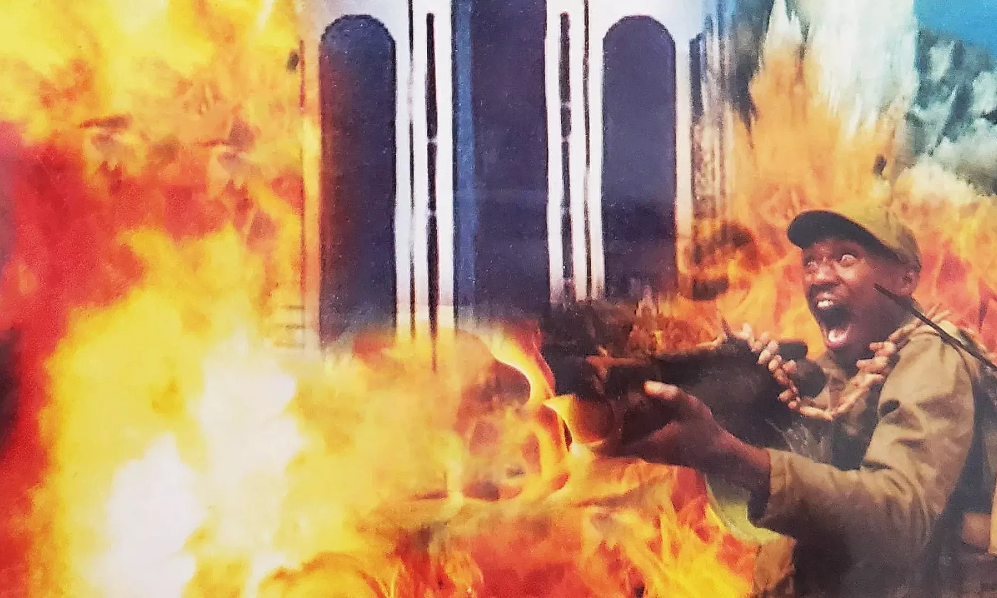 A soldier in a green uniform holding a gun, mouth open in shock or fear, surrounded by intense orange flames with a tall building in the background engulfed in fire.