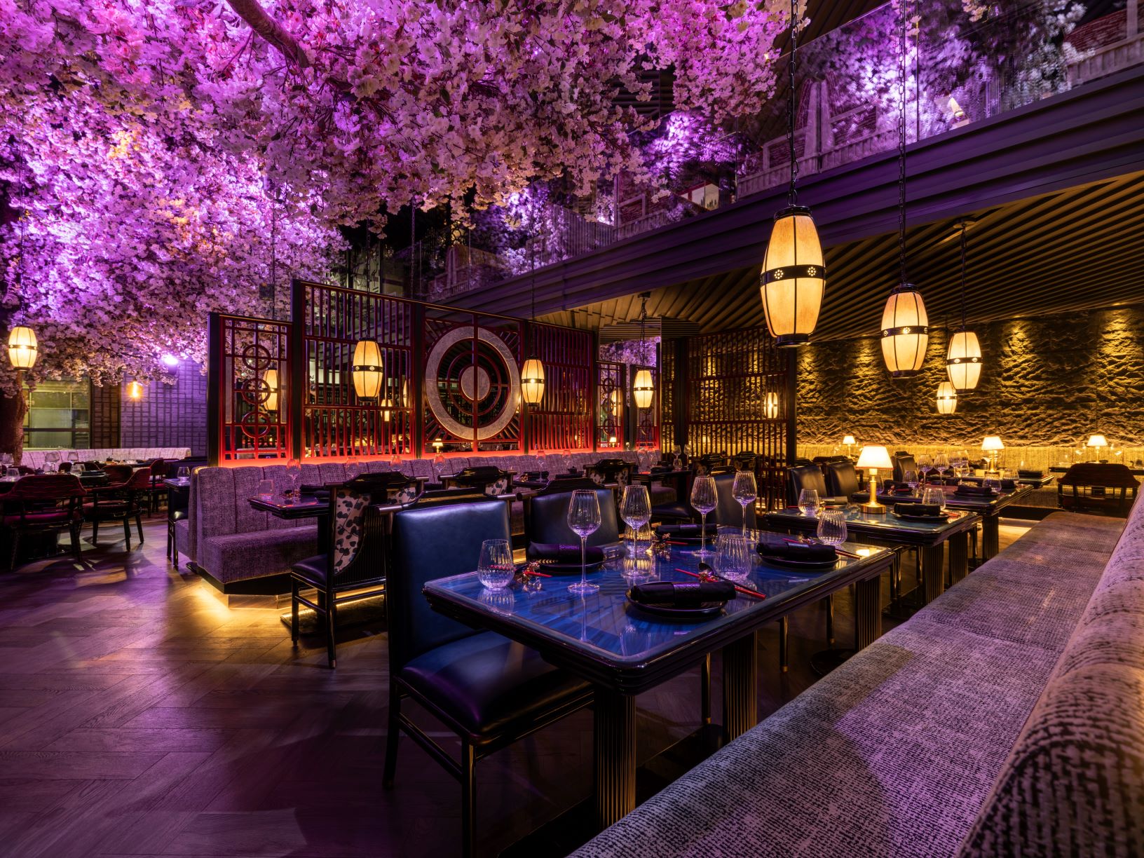 The interior of TATTU Leeds restaurant, featuring cherry blossom décor, warm purple lighting, and elegantly set dining tables.