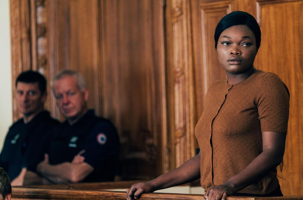 A woman stands in a courtroom, police officers stood in the background. 