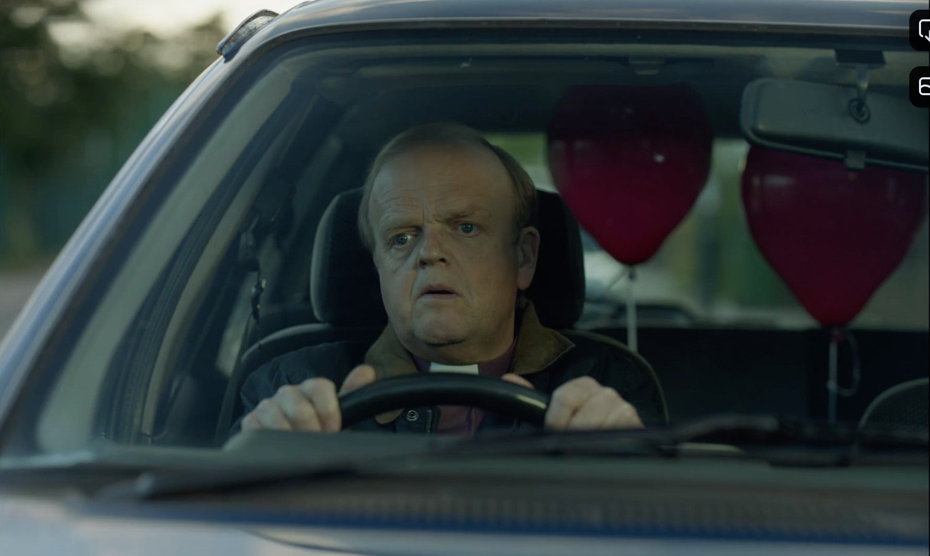 A man drives a car with red balloons floating in the back. 