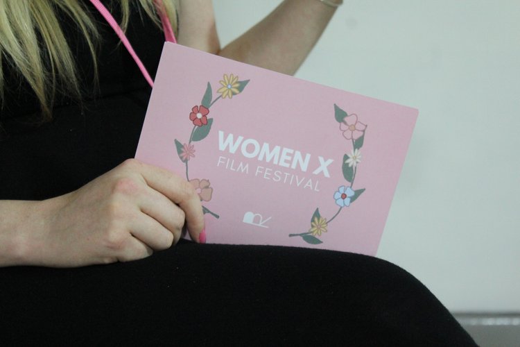 A woman's hands holding a pink flyer for the Women X Film Festival.  