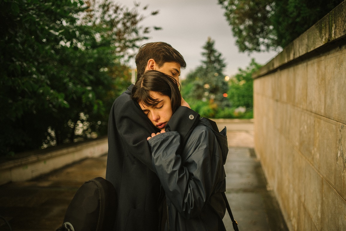 A young couple in school uniforms embrace tenderly. 