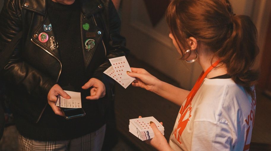 A photo of a LIFF Volunteer in branded clothing handing out audience response slips to a guest.