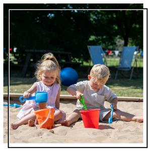 two children playing in a sand pit with buckets and spades