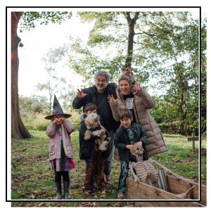Family dressed in Halloween costumes standing next to a skeleton in a coffin