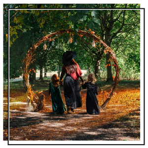 a woman and two children wearing witch costumes walking through a willow arch