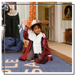 a child dressing up at temple newsam with a red jacket and big straw hat