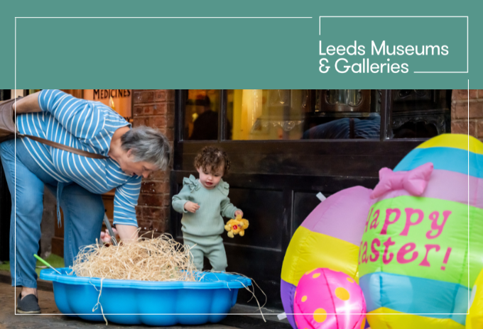 adult and child searching for eggs in the victorian streets at abbey house museum. the child is carrying a cuddly toy duck. large inflatable eggs saying 'happy easter'