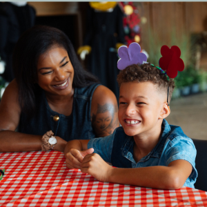 A child wearing a crafted floral headband and an adult sat together at a clothed table