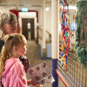 A child and an adult looking at an exhibition stand covered in felted artwork