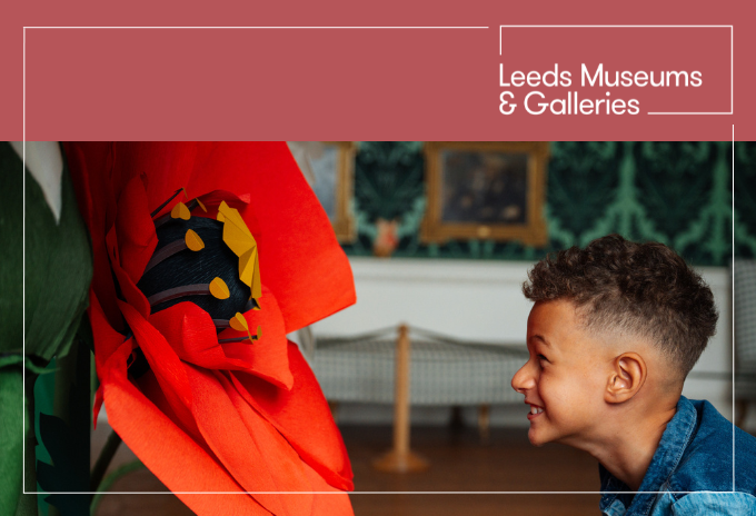 A profile of a child with a huge smile looking closely at a giant paper poppy sculpture