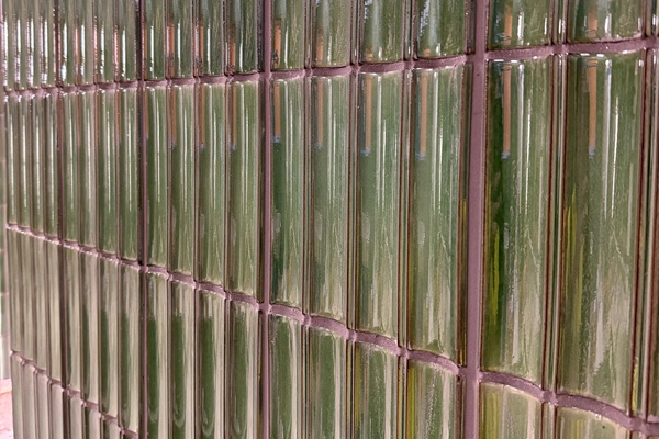 Close up of glossy green square tiles on the wall with dark grey grout in between.