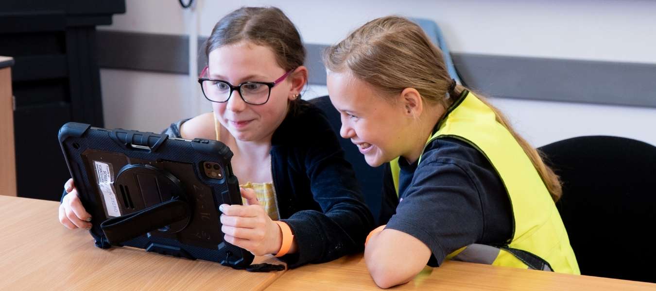 A photo showing two girls at Movie Club holding an ipad as part of an editing workshop.