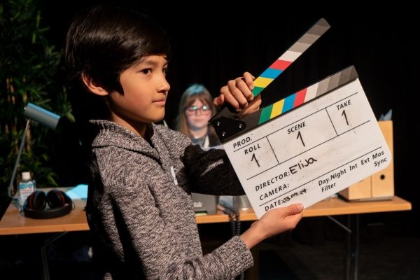 A young boy holds a clapperboard in front of a 'film set' as part of a Movie Club workshop.