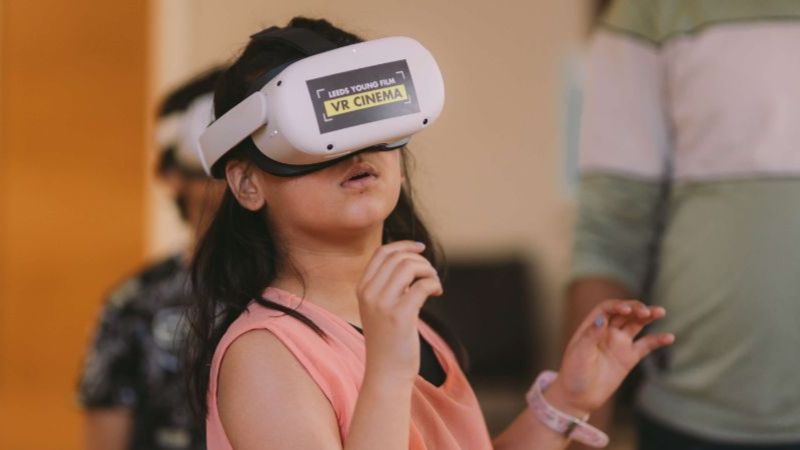 A young girl wears a VR headset and holds her hands up near her face.