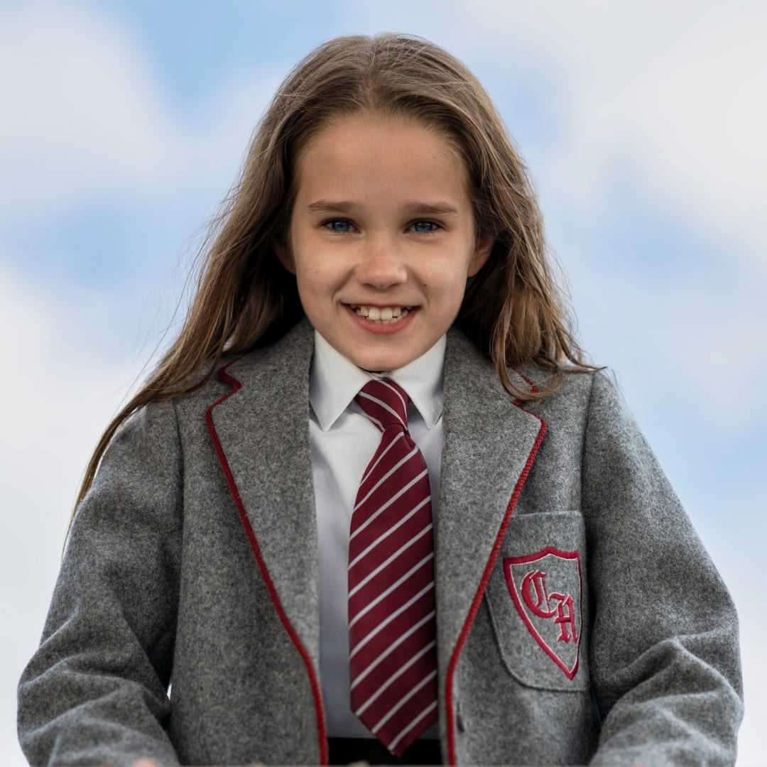 A young girl in a school uniform smiles.