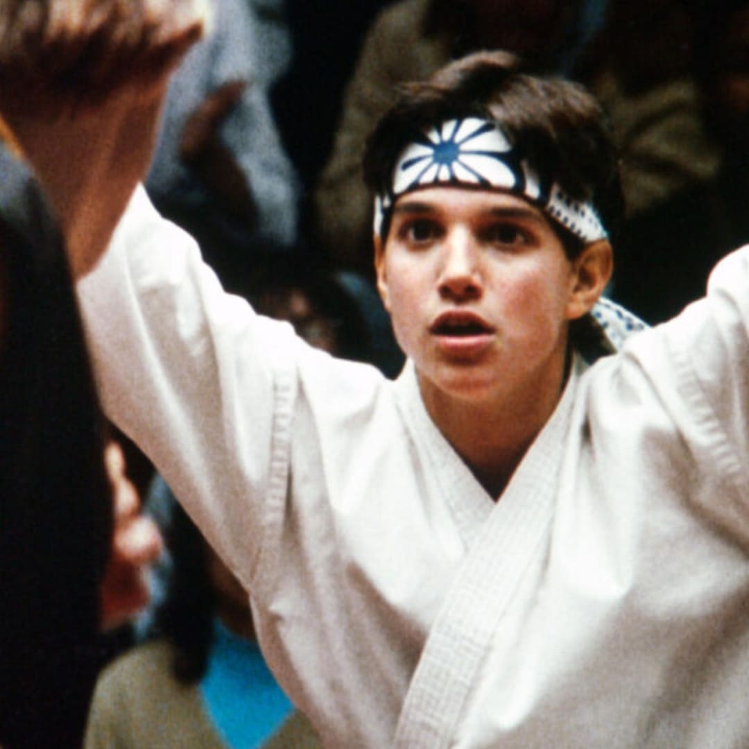 A young boy wears a traditional karate uniform: a white robe and a blue headband.
