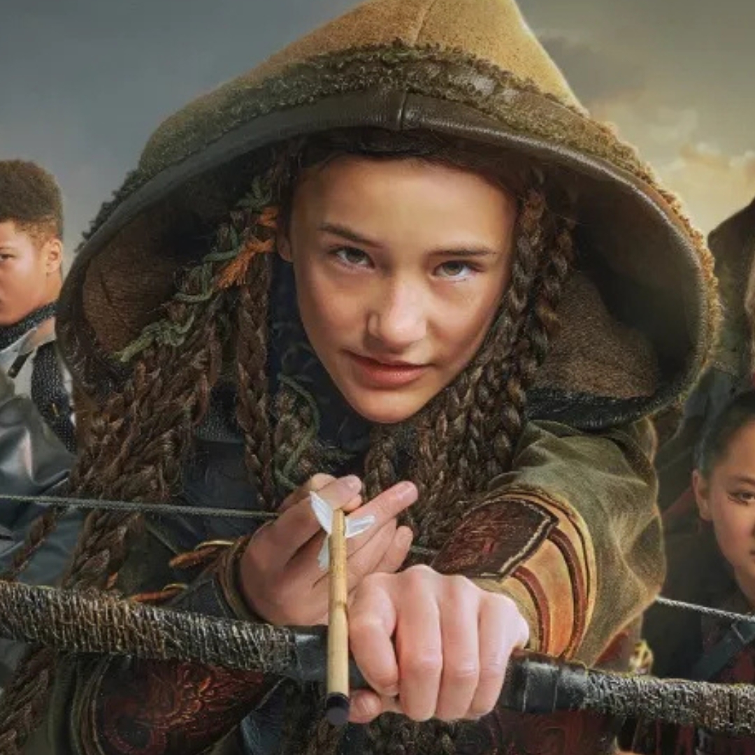 A girl with braided hair and a hood points a bow and arrow towards the camera