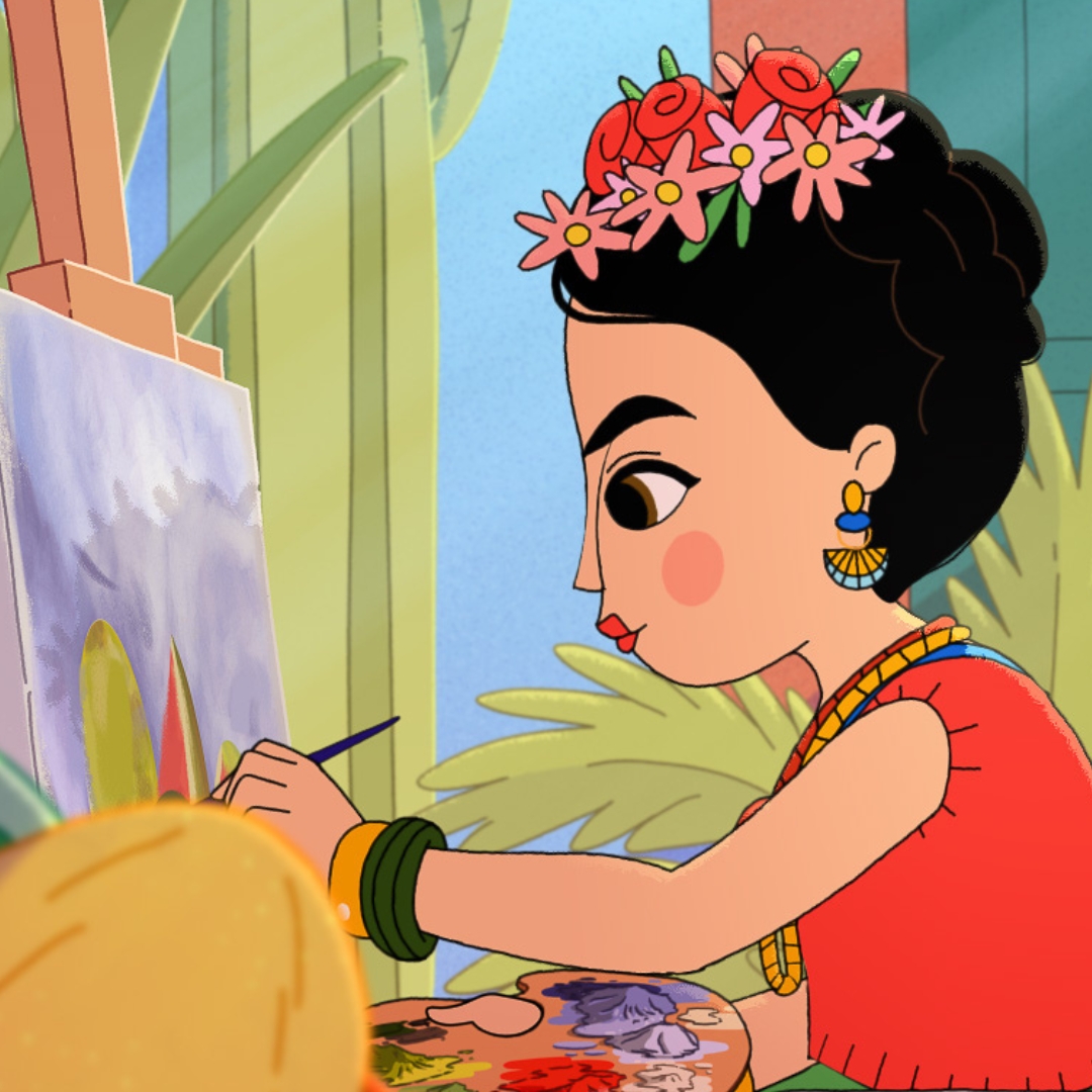 An animated depiction of Frida Kahlo sits in a wheelchair, painting a still life onto a canvas. She is wearing a floral headpiece and surrounded by plants, fruit and paintbrushes.