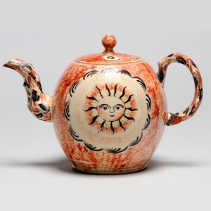 A close up image of a historic tea pot decorated with a sunshine with a face