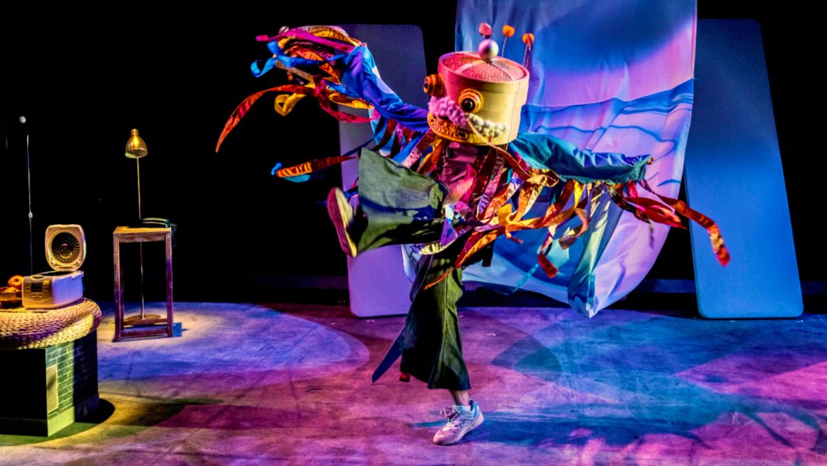 A man in puppet costume dances across a purple stage