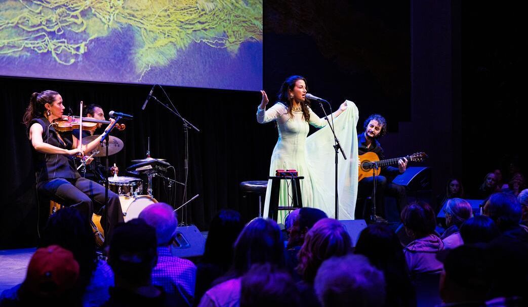 Woman in a long green pastel dress singing with three musicians at the Atrium