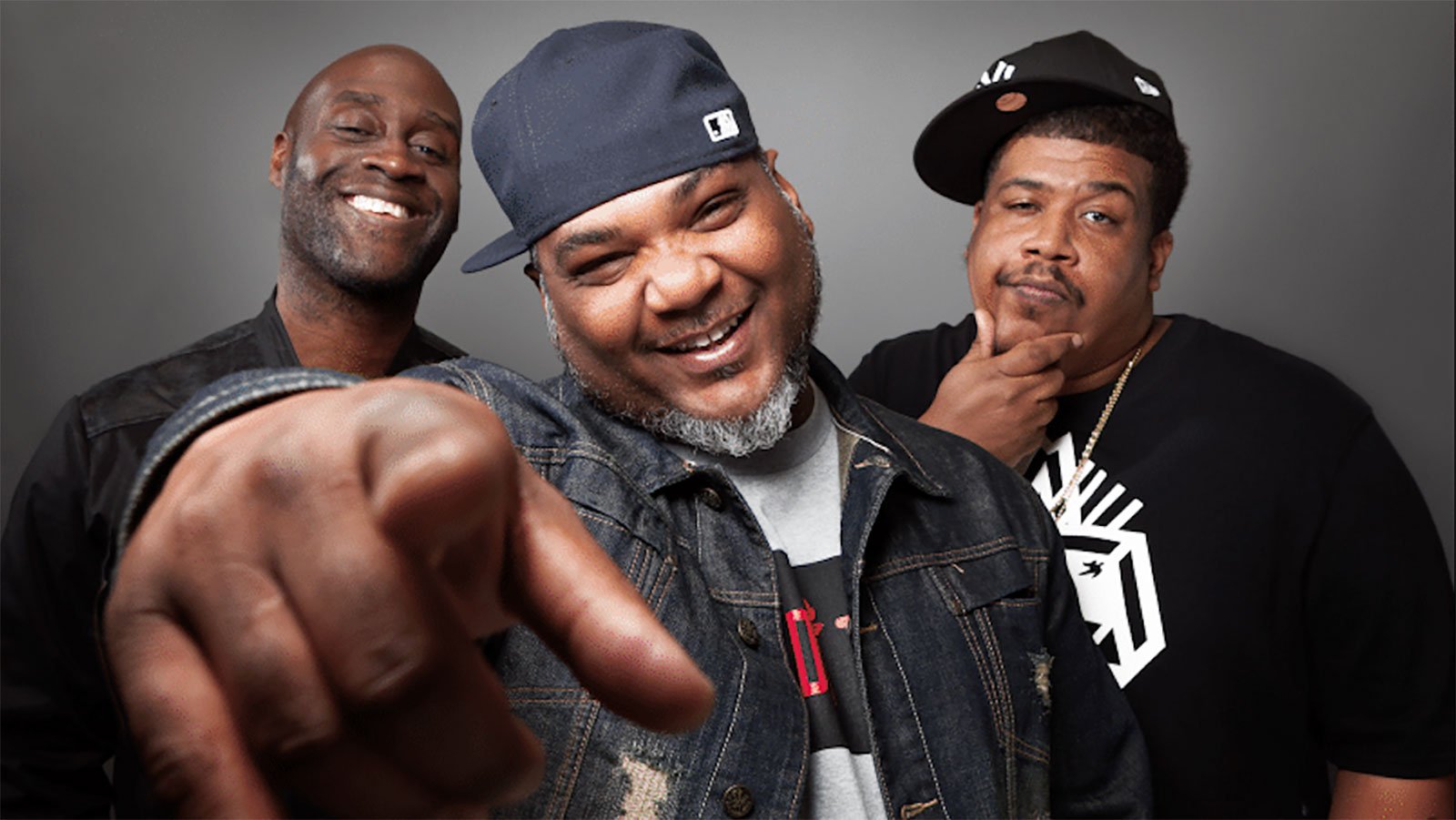Three black men smiling and posing in front of a grey wall